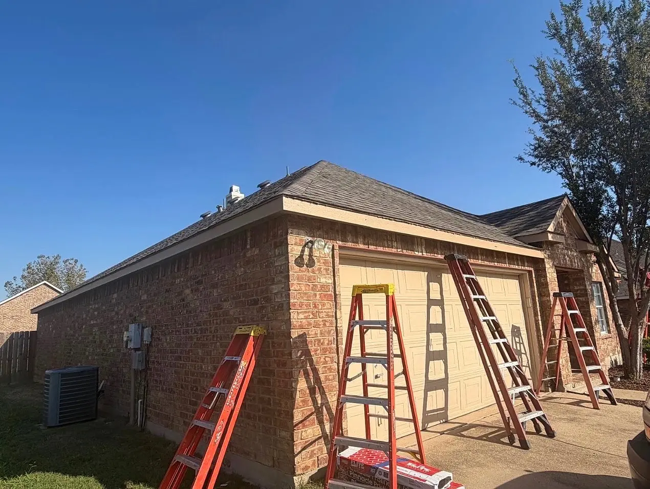 Side of a brick home with no gutters, ladders against the wall