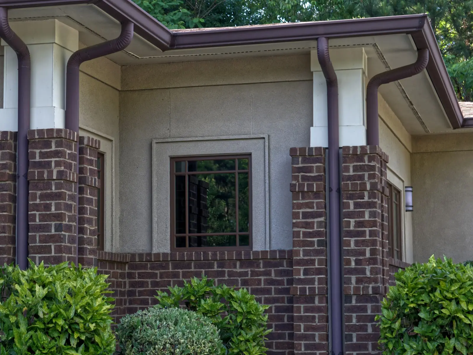 Brown seamless gutters with round downspouts on a brick and stucco home